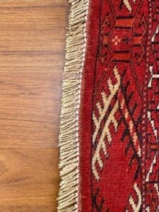 Un tappeto rosso con frange su un pavimento in legno.
