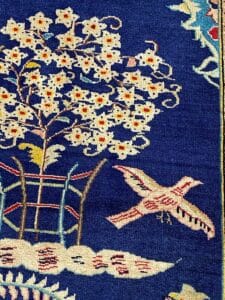 Un tappeto blu ornato con uccelli e fiori dal disegno intricato.