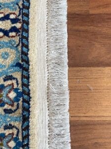 Primo piano di un tappeto Nain 168 blu e bianco su un pavimento di legno.