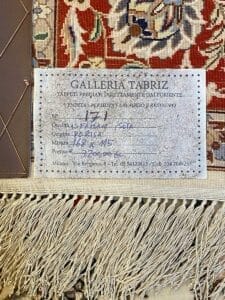 Un primo piano di un'etichetta della Galleria Tabriz, che descrive in dettaglio la pulizia e il restauro di un tappeto seta con informazioni su qualità, dimensioni e prezzo.