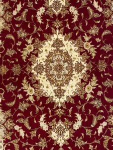 Intricati motivi floreali dorati su uno sfondo rosso intenso di un tessuto o un tappeto decorato, che mostrano la precisione del disegno automatico.
