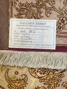 Etichetta su un tappeto persiano della "Galleria Tabriz" che descrive i servizi di vendita, scambio e restauro, con informazioni sulla qualità, origine, dimensione e prezzo del tappeto.