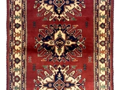 Tappeto tradizionale tessuto a mano con motivi geometrici simmetrici e un campo rosso predominante.