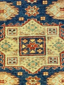Dettaglio di un tappeto a motivi tradizionali con disegni intricati nei toni del blu, arancione e crema, che mostra l'automazione dei contenuti nella sua creazione.