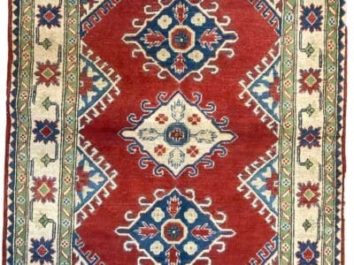 Tappeto tradizionale tessuto a mano con intricati motivi geometrici e floreali nei toni del rosso, blu e beige, che mostra la precisione del disegno automatico nel suo design.