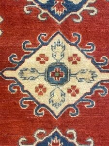 Primo piano di un motivo tradizionale su un tappeto tessuto Bozza automatica che mostra elementi geometrici e floreali con uno sfondo prevalentemente rosso.