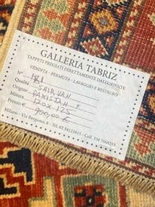 Un'etichetta della Galleria Tabriz su un tappeto a motivi riporta informazioni sulla qualità, l'origine, le dimensioni e i dettagli di contatto del venditore del tappeto.