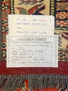 Un'etichetta della Galleria Tabriz, che ora include un dettaglio automatico, attaccato a un pezzo tessile, che indica specifiche come la qualità dell'arte, l'origine, il prezzo e le informazioni di contatto della galleria.
