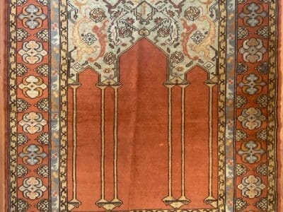 Un tappeto tradizionale e decorato con un campo rosso centrale e una bozza automatica decorativa che mostra motivi intricati.