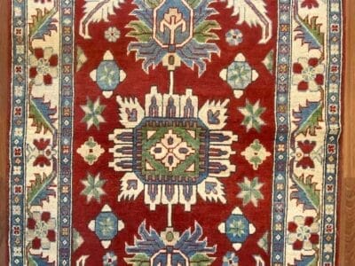 Tappeto a motivi tradizionali con disegni geometrici e floreali nei colori rosso, blu e crema.