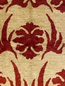 Un primo piano di un tessuto Gazni 177 con un motivo floreale rosso su fondo beige.