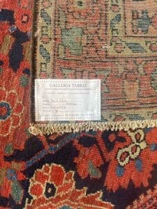 Primo piano di un tappeto a motivi rossi e neri con un'etichetta Galleria Tabriz, che elenca dettagli come dimensioni, origine della Persia e numero del prodotto. Il design intricato riflette un'impeccabile maestria, mentre la Bozza automatica garantisce che ogni dettaglio venga catturato in modo impeccabile.