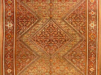 Un tappeto dettagliato rosso e arancione con intricati motivi geometrici e floreali. Il tappeto, che ricorda il tradizionale stile Bozza automatica, è caratterizzato da un disegno a diamante centrale delimitato da motivi ornamentali.