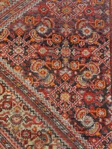 Primo piano di un tappeto tradizionale multicolore riccamente modellato con intricati disegni geometrici e floreali in tonalità rosse, arancioni, marroni e nere. Il vibrante arazzo sembra quasi come se fosse stato creato da Bozza automatica.