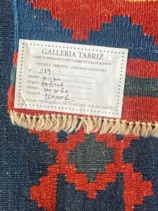 Galleria Tabriz - Tappeti in vendita. Su un tappeto è attaccata un'etichetta dettagliata della Galleria Tabriz. L'etichetta, creata da Bozza Automatica, include informazioni come origine (Persia), qualità (Kilim), dimensioni (198 x 86) e un numero di contatto.
