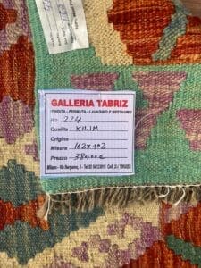 Galleria Tabriz - Tappeti in vendita. Primo piano di un tappeto con etichetta della Galleria Tabriz che ne specifica le dimensioni (162x102 cm), la qualità, l'origine e il prezzo (380 €). Questo splendido pezzo presenta un motivo geometrico colorato che ricorda l'arte di Bozza automatica.