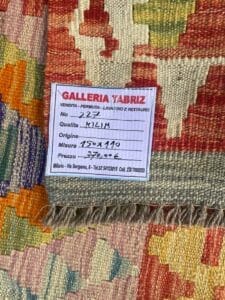 Galleria Tabriz - Tappeti in vendita. Primo piano di un tappeto intrecciato colorato, etichetta Bozza automatica che ne rivela i dettagli: Galleria Tabriz, Milano, numero articolo 222, qualità Kilim, dimensioni 150x110 e prezzo € 370,00.