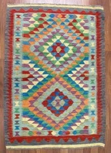 Galleria Tabriz - Tappeti in vendita. Un tappeto colorato con motivi geometrici a forma di rombi nei toni del rosso, blu, verde, giallo e arancione dona vitalità al pavimento in legno, creando una bozza automatica dalla consistenza vibrante e calda.