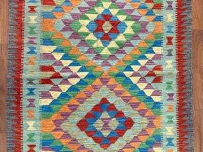 Galleria Tabriz - Tappeti in vendita. Un tappeto colorato con motivi geometrici a forma di rombi nei toni del rosso, blu, verde, giallo e arancione dona vitalità al pavimento in legno, creando una bozza automatica dalla consistenza vibrante e calda.