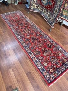 Galleria Tabriz - Tappeti in vendita. Un tappeto orientale rosso con intricati motivi floreali impreziosisce il pavimento in legno, aggiungendo un tocco di eleganza Bozza. Altri tappeti, forse scelti con un occhio altrettanto attento, sono visibili sullo sfondo.