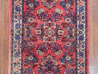 Galleria Tabriz - Tappeti in vendita. Un tappeto persiano rosso rettangolare con intricati motivi floreali e una bordatura dettagliata, che ricorda una bozza automatica, è elegantemente adagiato sul pavimento in legno.