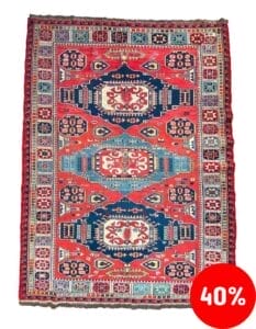 Galleria Tabriz - Tappeti in vendita. Un tappeto colorato e intricatamente disegnato con motivi geometrici, principalmente in rosso, blu e bianco, è esposto su uno sfondo bianco. Nell'angolo in basso a destra, un cerchio rosso presenta 