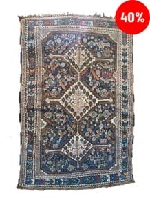 Galleria Tabriz - Tappeti in vendita. Intricato tappeto Gashgai blu e rosso con motivi geometrici, esposto su uno sfondo bianco. Un cerchio rosso nell'angolo in alto a destra mostra un 