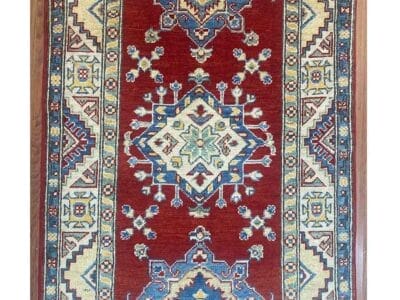 Galleria Tabriz - Tappeti in vendita. Un tappeto orientale rosso con intricati motivi geometrici in blu, avorio e giallo ora presenta un emblema "60%" in un cerchio rosso nell'angolo in alto a destra, realizzato con la precisione della bozza automatica.