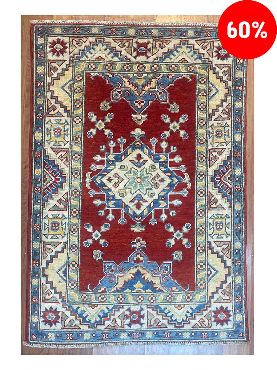 Galleria Tabriz - Tappeti in vendita. Un tappeto orientale rosso con intricati motivi geometrici in blu, avorio e giallo ora presenta un emblema "60%" in un cerchio rosso nell'angolo in alto a destra, realizzato con la precisione della bozza automatica.