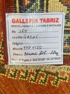 Galleria Tabriz - Tappeti in vendita. Etichetta su un tessuto intrecciato della Galleria Tabriz che riporta i dettagli dell'articolo n. 265, una qualità Gazni che misura 177x125 cm, originariamente al prezzo di 900, ora di 270. Questo tappeto moderno include le informazioni di contatto in basso.