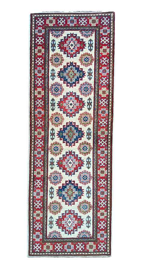 Galleria Tabriz - Tappeti in vendita. Un tappeto decorativo rettangolare con motivi geometrici e bordi rossi, blu e bianchi presenta una serie di medaglioni allineati al centro, che conferiscono un tocco di bozza automatica.