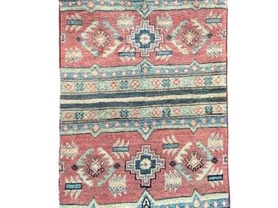 Galleria Tabriz - Tappeti in vendita. Un tappeto rettangolare kazak con motivi geometrici nelle tonalità del rosso, blu e beige, che mettono in risalto motivi simmetrici e strisce orizzontali.