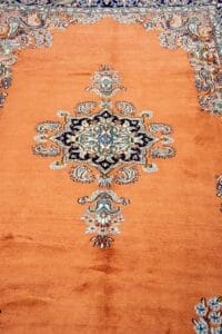 Galleria Tabriz - Tappeti in vendita. Tappeto arancione ornato con un dettagliato medaglione floreale centrale e intricati disegni sui bordi blu e crema.