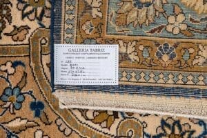 Galleria Tabriz - Tappeti in vendita. Primo piano di un tappeto a fantasia con etichetta della Galleria Tabriz che riporta dettagli sulla provenienza e sulle dimensioni, evidenziando l'eleganza tipica di un Tappeto Qum proveniente dalla Persia.