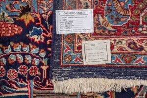 Galleria Tabriz - Tappeti in vendita. Primo piano delle etichette di un tappeto persiano che mostrano l'origine, le dimensioni e le informazioni sul produttore su uno sfondo colorato, che mette in evidenza questo Tappeto Mashad autentico proveniente dalla Persia.