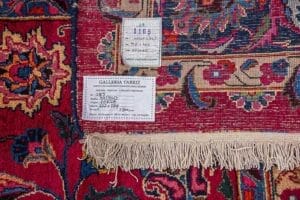 Galleria Tabriz - Tappeti in vendita. Primo piano di un angolo di tappeto Tappeto Mashad, con etichette con dettagli dell'articolo e bordo sfrangiato.