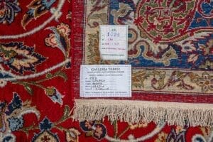 Galleria Tabriz - Tappeti in vendita. Primo piano dell'angolo di un tappeto Tappeto Isfahan che mostra le etichette con i dettagli e il motivo decorativo rosso, blu e beige tipico della Persia Tappeto.