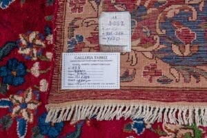 Galleria Tabriz - Tappeti in vendita. Primo piano di un tappeto Tappeto Kirman a motivi persiani con due etichette, una scritta a mano e una stampata, contrassegnate dal numero 288 posto sopra di essa.