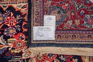 Galleria Tabriz - Tappeti in vendita. Primo piano di un angolo di tappeto persiano, che mostra motivi colorati e due etichette con dettagli scritti a mano e stampati: uno squisito esempio di artigianato Tappeto Saruk.
